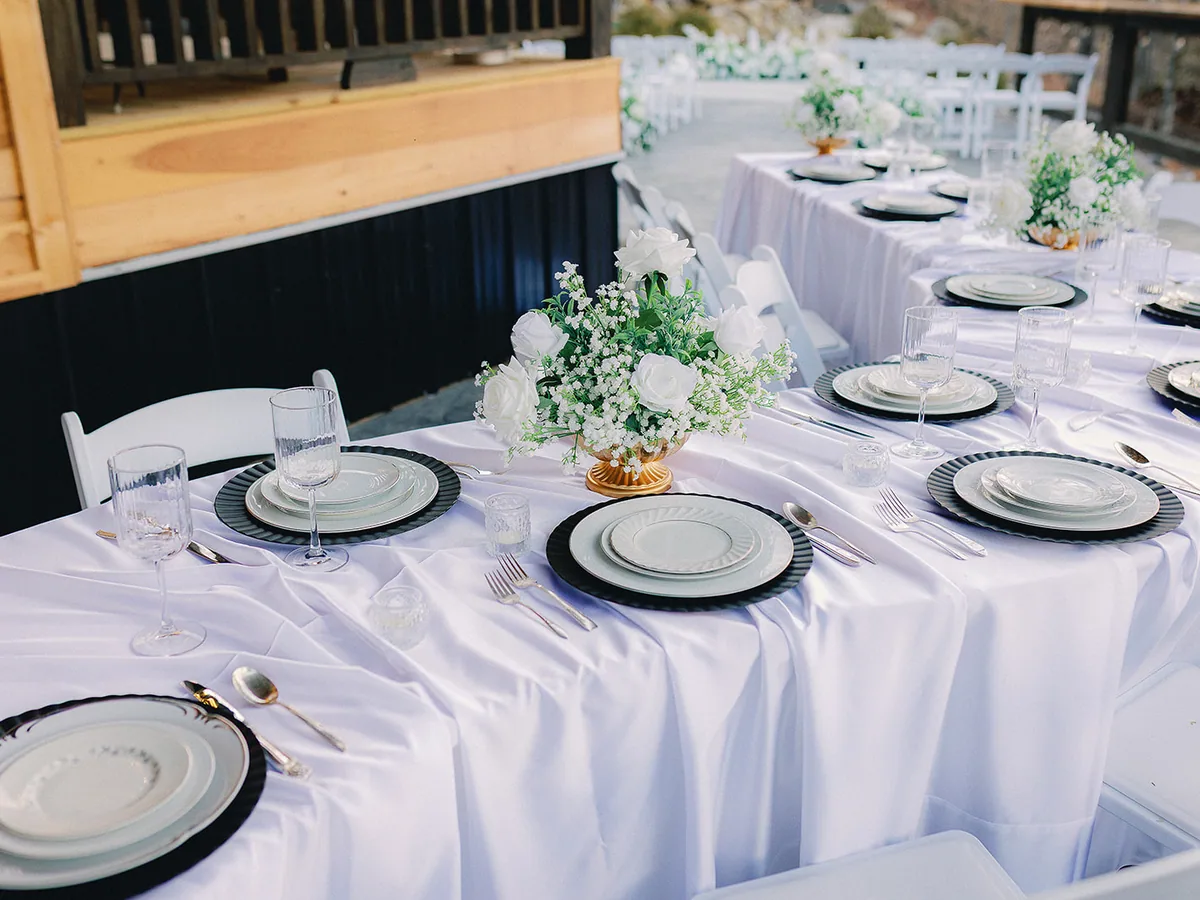 A long table laid with white linen, black chargers and greenery