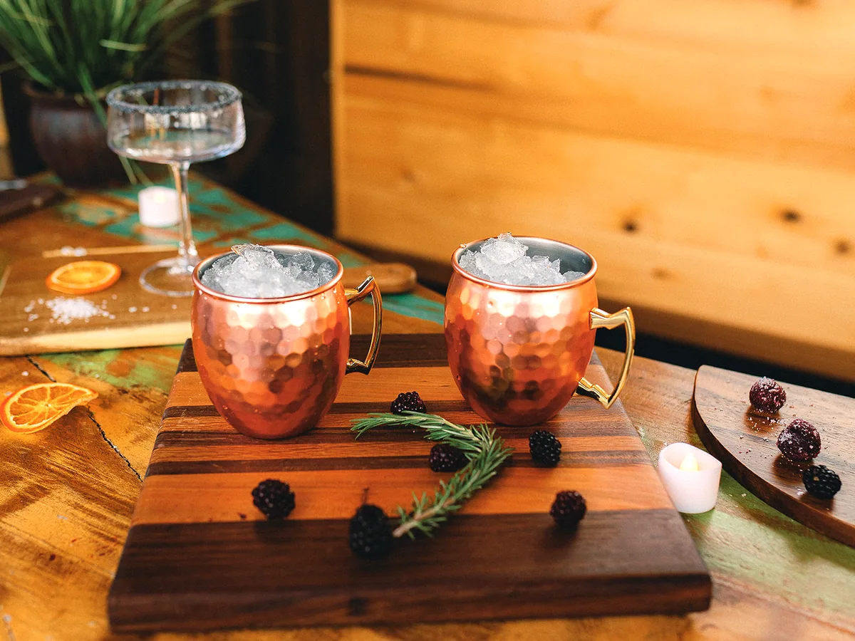 Copper mugs and a garnished cocktail on a wooden board