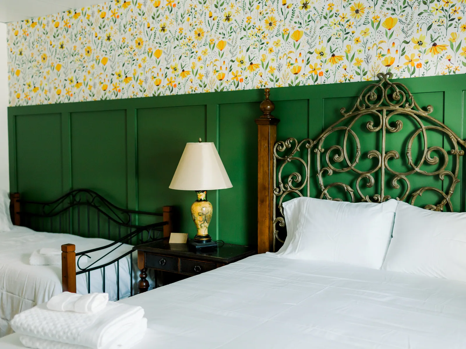A bedroom with two beds, green panelling and a wrought-iron headboard