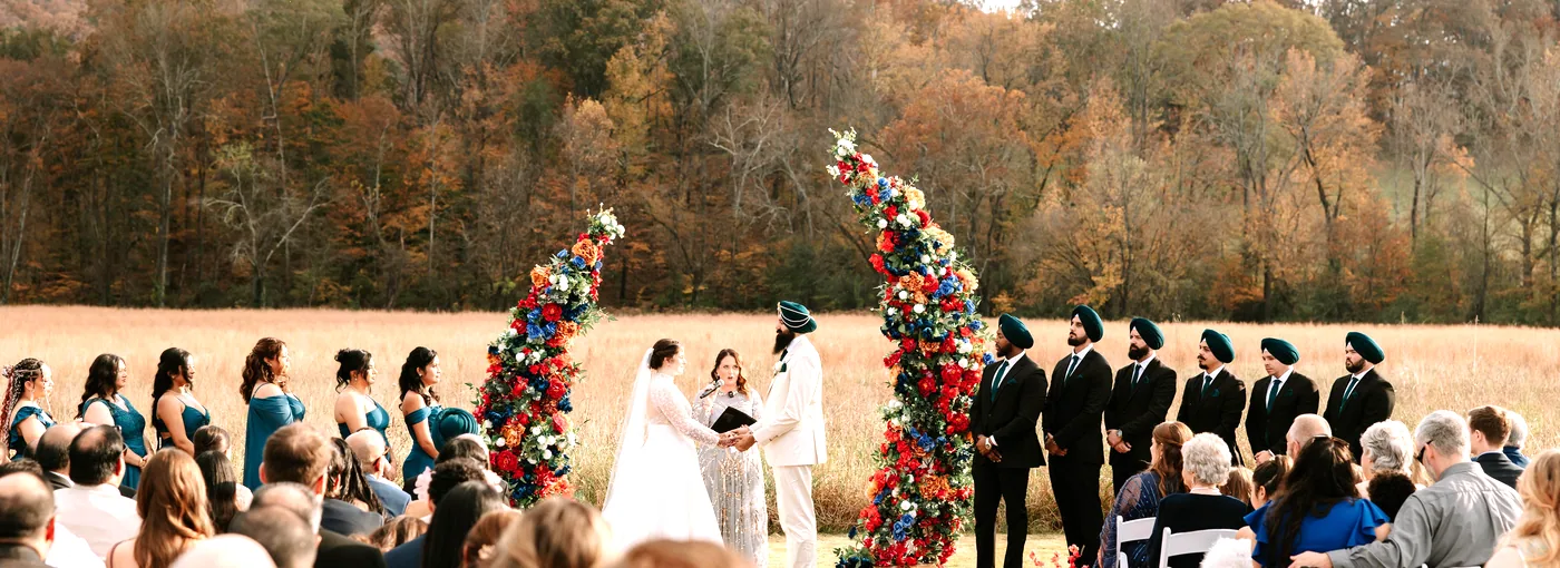 Caitlin and Gupinder marry in the meadow in autumn, the congregation seated toward the ridge